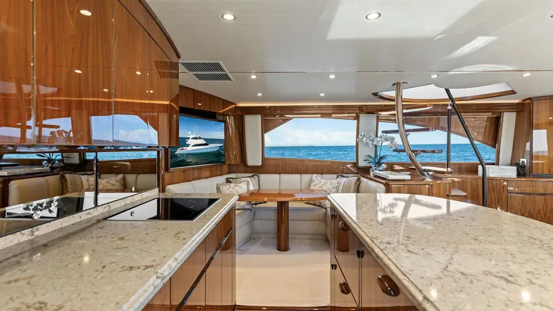 Slide: The Image of Salon with Panoramic Ocean Views The salon of the 2018 Viking 62 Enclosed Bridge features luxurious finishes with high-gloss wood cabinetry and elegant marble countertops. Expansive windows provide breathtaking panoramic views of the ocean, enhancing the spacious feel of the interior. Co - 7751226