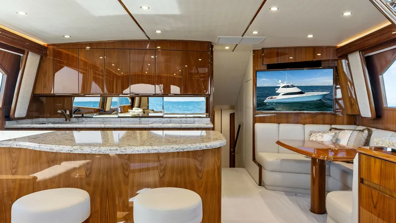 Slide: The Image of Spacious Salon with Dinette and Galley This elegant salon on the Viking 62 Enclosed Bridge features a modern galley with a sleek granite countertop and polished wood cabinetry. The comfortable dinette offers ample seating, perfect for dining or entertaining while enjoying panoramic views throu - 7751224