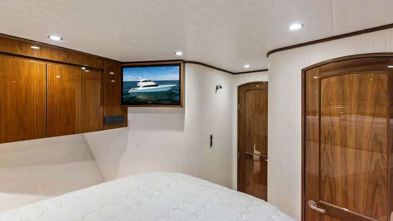 Slide: The Image of Master Stateroom with TV The master stateroom of the 2018 Viking 62 Enclosed Bridge features elegant wood cabinetry and a plush, comfortable bed. A flat-screen TV is strategically placed for optimal viewing, enhancing the entertainment experience. The polished wood finishes and s - 7751252