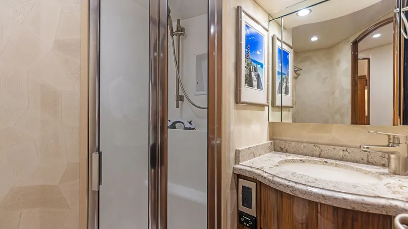 Slide: The Image of Elegant En-Suite Bathroom This en-suite bathroom on the Viking 62 Enclosed Bridge features a sleek, modern design with a glass-enclosed shower. The elegant marble countertop and rich wood cabinetry add a touch of luxury. Soft recessed lighting enhances the ambiance, while framed a - 7751266
