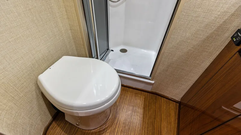Slide: The Image of Elegant Ensuite Head with Shower This well-appointed ensuite head features a sleek, modern design with a compact toilet and a glass-enclosed shower. The rich wood flooring and textured wall coverings add warmth and elegance to the space. Ideal for comfort and convenience, this private ar - 7751256