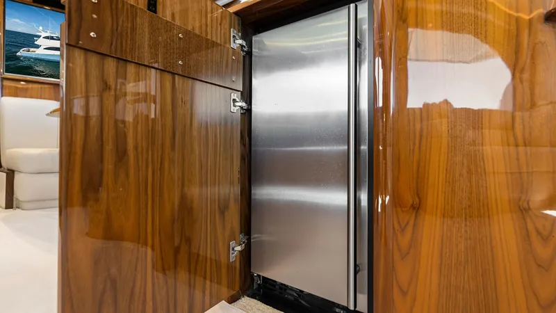 Slide: The Image of Galley Refrigerator with Wood Finish This image showcases the sleek stainless steel refrigerator set within beautifully crafted wood cabinetry aboard the Viking 62 Enclosed Bridge. The rich, high-gloss wood finish adds warmth and elegance to the galley area. The design seamlessly integrates - 7751231