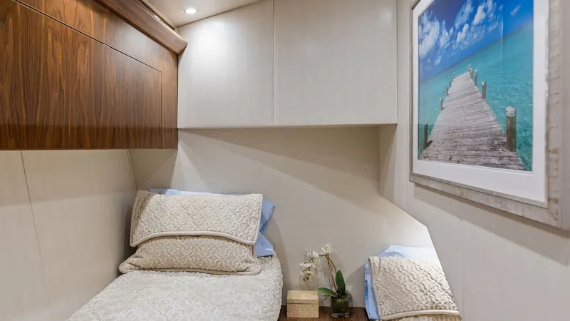 Slide: The Image of Cozy Guest Stateroom This inviting guest stateroom on the 2018 Viking 62 Enclosed Bridge offers a comfortable twin berth setup with plush bedding. The room features elegant wood cabinetry and soft ambient lighting, creating a warm and relaxing atmosphere. A scenic artwork add - 7751269