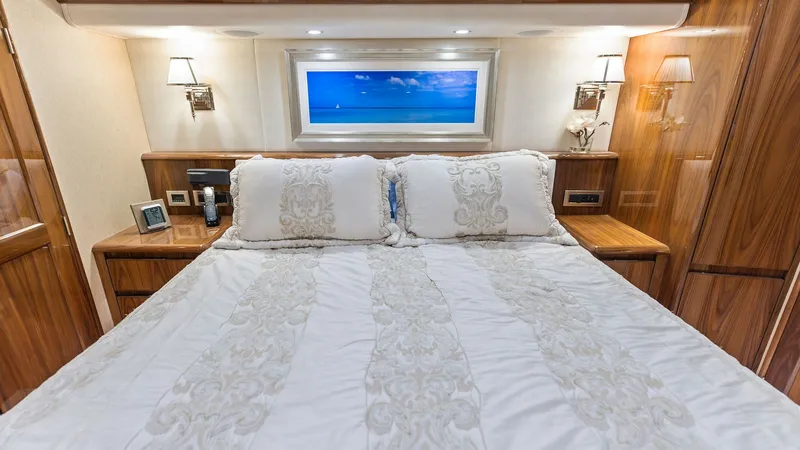 Slide: The Image of Luxurious Master Stateroom with Window View This master stateroom aboard the Viking 62 Enclosed Bridge exudes luxury with its sumptuous bedding and elegant wood finishes. The room features built-in bedside tables and ambient wall lighting, creating a warm and inviting atmosphere. A large window off - 7751237