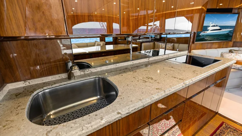 Slide: The Image of Galley with Polished Wood Finish The galley of the Viking 62 Enclosed Bridge features elegant wood cabinetry and a sleek, polished countertop. A modern stainless steel sink is complemented by ample workspace, ideal for meal preparation. The mirrored backsplash adds depth and sophisticati - 7751230