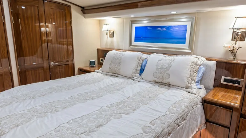 Slide: The Image of Luxurious Master Stateroom Interior This elegant master stateroom on the 2018 Viking 62 Enclosed Bridge features a plush, king-size bed adorned with intricate bedding. The space is accented by rich wood finishes and ample natural light, creating a warm and inviting atmosphere. A large frame - 7751235