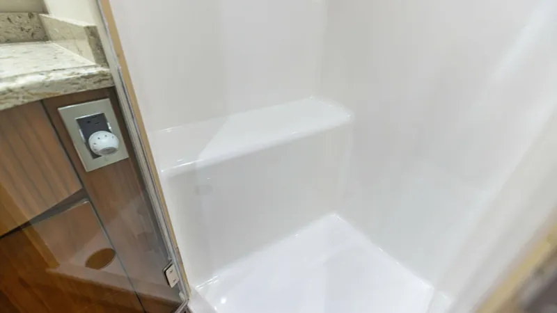Slide: The Image of Enclosed Shower with Granite Accents This image showcases a sleek, enclosed shower on the Viking 62 Enclosed Bridge. The shower features a white, easy-to-clean surface with a convenient built-in seat, offering both practicality and comfort. Adjacent to the shower, the granite countertop and - 7751243