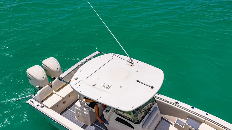 Slide: The Image of Aerial View of Helm and Aft Deck This image showcases the helm and aft deck of the 2024 Grady-White 281 CE. The sleek hardtop provides shade and protection, while the spacious deck features comfortable seating with easy access to the twin outboard engines. The boat's elegant design and r - 7766863