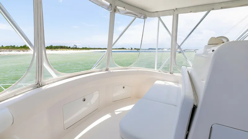 Slide: The Image of Flybridge Seating Area with Ocean View This image showcases the flybridge seating area of the 2003 Cabo 43 Convertible, 'Chao Bella'. The space features comfortable cushioned seating with ample storage beneath, enclosed by clear panels offering panoramic ocean views. The bright and airy ambian - 7831807