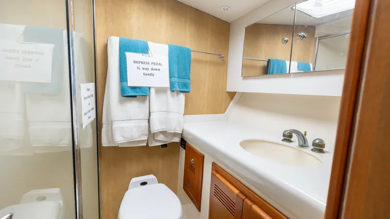 Slide: The Image of Elegant Onboard Bathroom This well-appointed bathroom on the 2003 Cabo 43 Convertible features a sleek vanity with ample counter space and a polished sink. The room is accented by warm wood cabinetry and a spacious mirror, enhancing the airy feel. Modern fixtures and neatly arran - 7831800