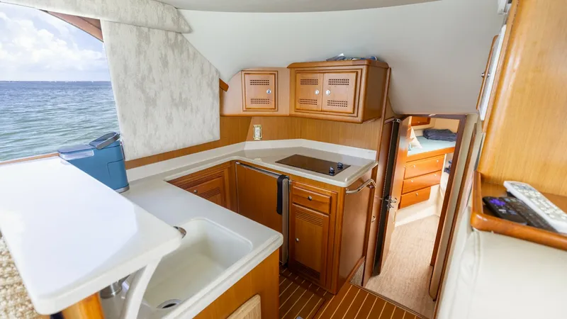 Slide: The Image of Galley and Cabin Entrance View This image showcases the inviting galley of the 2003 Cabo 43 Convertible, featuring a well-equipped kitchen with a sleek countertop and built-in sink. The warm wooden cabinetry provides ample storage, complementing the elegant teak flooring. The open layo - 7831793