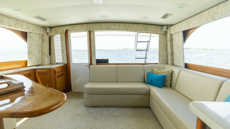Slide: The Image of Spacious Interior Salon with Aft View This inviting salon on the 2003 Cabo 43 Convertible, 'Chao Bella,' features a generously sized L-shaped sofa with plush upholstery, perfect for relaxation. Large windows and a glass door provide panoramic views of the surrounding water, enhancing the airy - 7831787