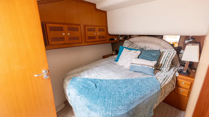 Slide: The Image of Cozy Forward Stateroom This inviting forward stateroom on the 2003 Cabo 43 Convertible features a plush double berth adorned with stylish bedding and ample pillows for comfort. Rich wooden cabinetry offers generous storage, while soft ambient lighting creates a warm, welcoming - 7831797