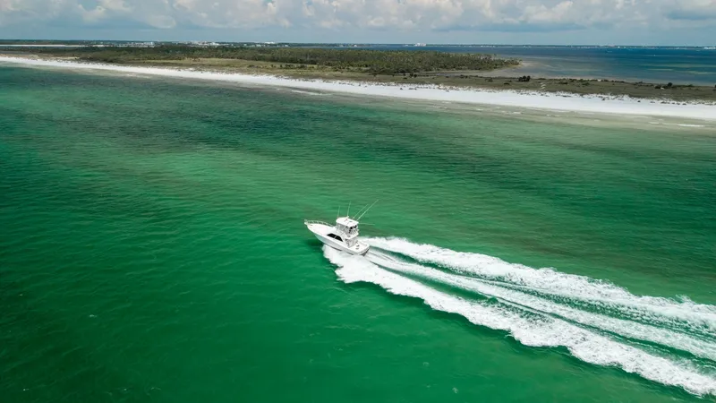 Slide: The Image of Aerial View of Chao Bella Cruising The 2003 Cabo 43 Convertible, Chao Bella, is captured in motion from an aerial perspective, showcasing its sleek design and powerful performance. The vessel cuts through the vibrant turquoise waters, leaving a trail of white wake behind. This dynamic view - 7831822