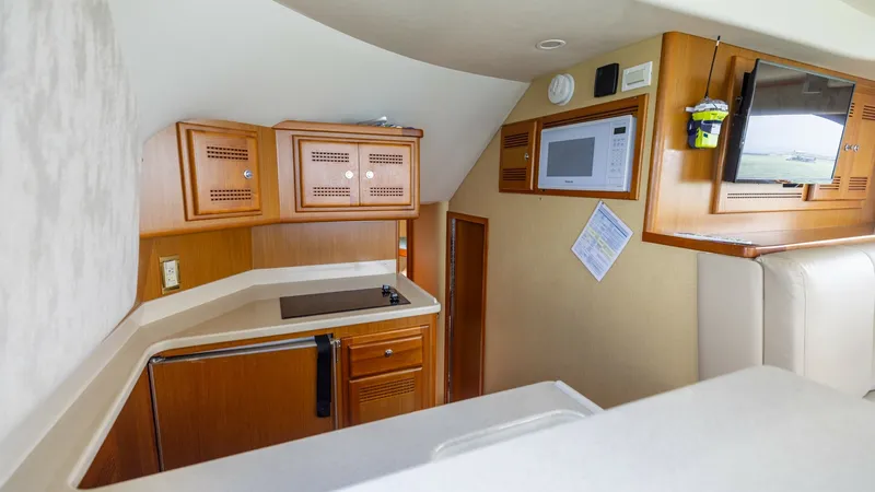 Slide: The Image of Galley with Wood Cabinetry The galley of the 2003 Cabo 43 Convertible, 'Chao Bella,' features elegant wood cabinetry and modern appliances, including a built-in microwave. The compact design maximizes space efficiency, with ample storage and a sleek countertop for meal preparation. - 7831794