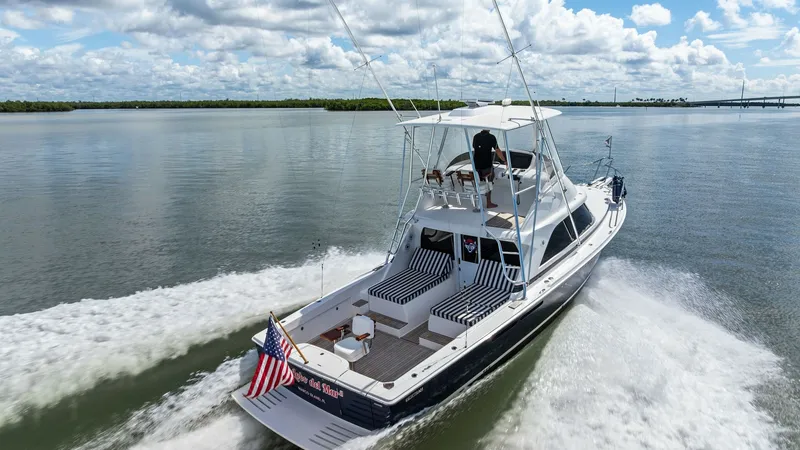 Slide: The Image of Aft Deck and Flybridge View This image showcases the aft deck of the 2019 Bertram 35 Flybridge, featuring comfortable seating with striped cushions perfect for relaxation. The flybridge above offers an elevated vantage point with additional seating and a helm station, providing exce - 7851553