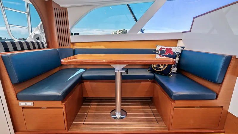 Slide: The Image of Flybridge Dinette with Panoramic View This inviting flybridge dinette features plush, blue upholstered seating and a polished wooden table, perfect for socializing or dining. Large windows provide a stunning panoramic view, enhancing the open and airy feel of the space. The elegant wood finis - 7851524