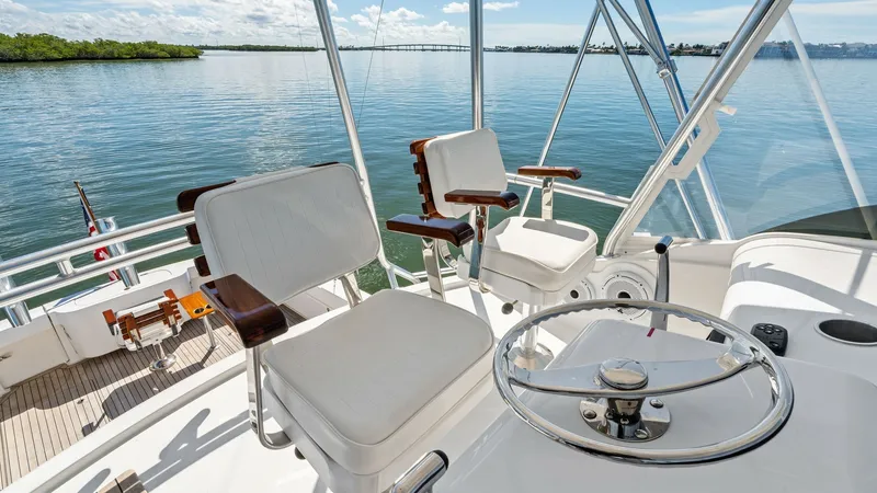 Slide: The Image of Flybridge Helm with Seating The flybridge of the 2019 Bertram 35 Flybridge offers a commanding view with dual helm chairs featuring plush white upholstery and polished wooden accents. The stainless steel steering wheel and clear instrumentation ensure precise navigation, while the e - 7851539