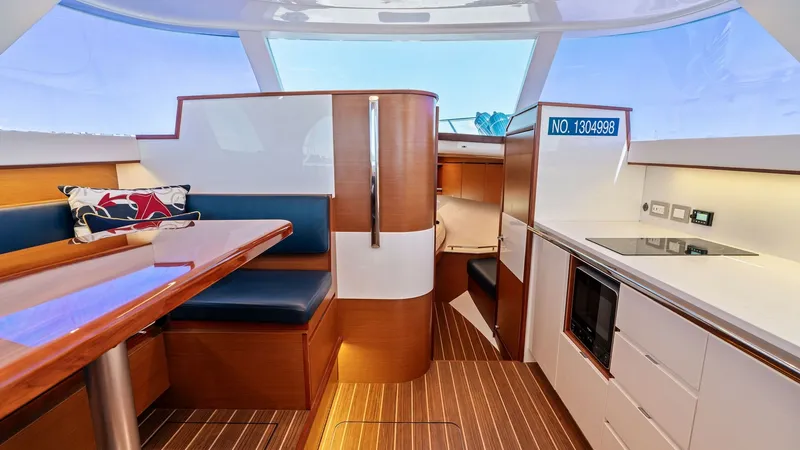 Slide: The Image of Interior Salon and Galley View This image showcases the stylish interior salon and galley of the 2019 Bertram 35 Flybridge. The space is elegantly appointed with rich wood finishes and a sleek, modern layout. The seating area offers comfort with plush cushions, while the well-equipped - 7851526