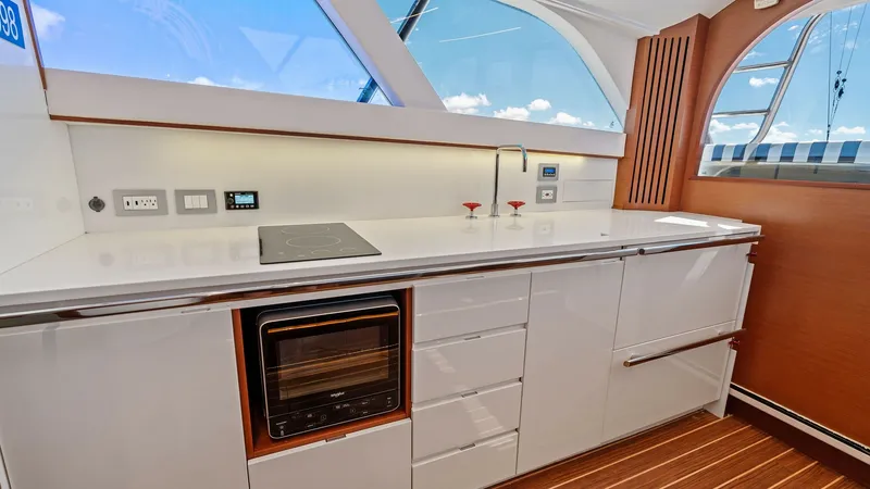 Slide: The Image of Modern Galley with Ocean Views This sleek and contemporary galley on the 2019 Bertram 35 Flybridge features high-gloss cabinetry and a streamlined countertop, equipped with a modern stovetop and built-in oven. Large windows flood the space with natural light and offer stunning ocean vi - 7851521