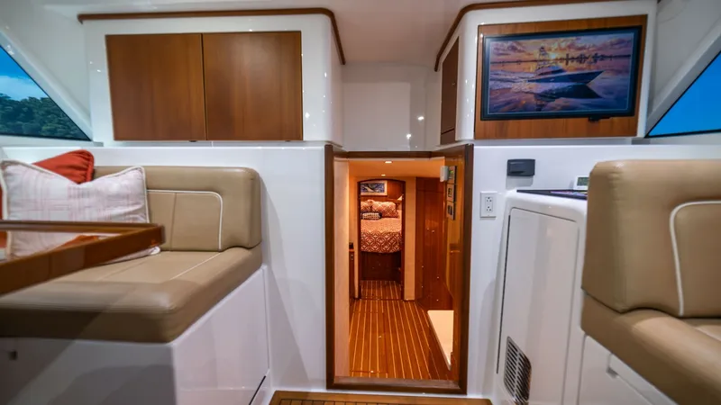Slide: The Image of Interior Seating and Cabin Access This image showcases the inviting interior of the 2020 Viking 46 BF, featuring plush seating with elegant stitching and a high-gloss wooden table. The cabinetry offers ample storage, while the passageway leads into a cozy cabin with warm ambient lighting. - 7854747