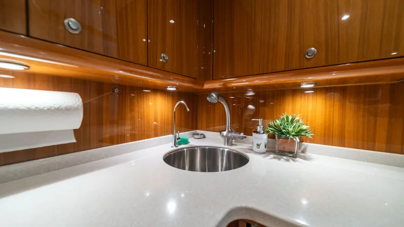 Slide: The Image of Galley with Polished Wood Finish This sleek galley showcases modern elegance with its polished wood cabinetry and soft ambient lighting. The smooth, white countertop offers ample space for meal preparation, while the stainless-steel sink and fixtures add a touch of sophistication. Practi - 7854754