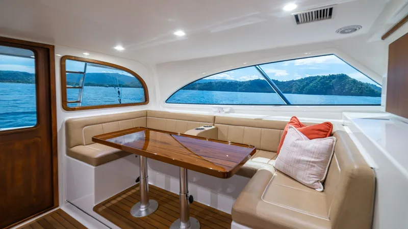 Slide: The Image of Saloon Seating with Ocean View The saloon of the 2020 Viking 46 BF offers a luxurious seating area with plush, cream-colored upholstery that complements the rich wood finishes of the table and paneling. Large windows provide panoramic ocean views, filling the space with natural light a - 7854750