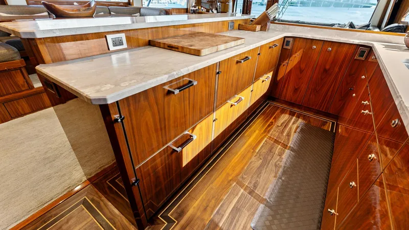 Slide: The Image of Galley with Custom Cabinetry The galley of the Viking 80 Convertible features exquisite custom cabinetry with a rich wood finish, offering ample storage space. The sleek countertops provide a functional workspace, complemented by high-end fixtures. Large windows flood the area with n - 7932656