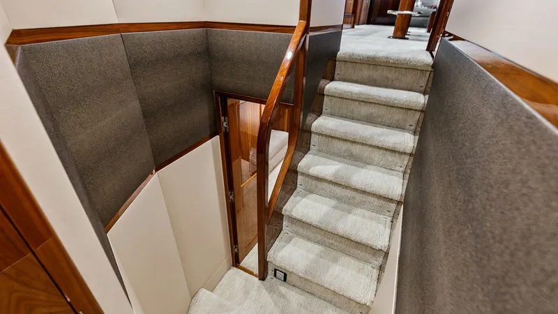 Slide: The Image of Elegant Interior Staircase This image showcases the elegant staircase within the Viking 80 Convertible, featuring plush carpeted steps and rich wood accents. The design provides a seamless transition between decks, enhancing the yacht's luxurious interior. The combination of soft n - 7932661
