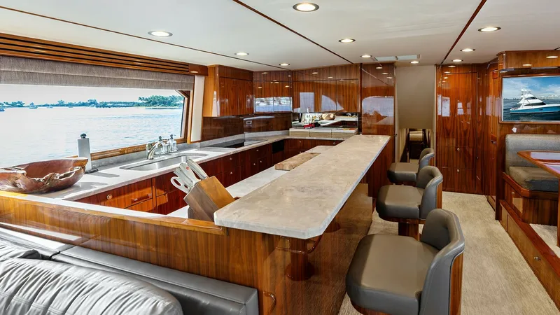 Slide: The Image of Spacious Galley with Bar Seating This elegant galley on the 2017 Viking 80 Convertible features a sleek countertop with bar seating, ideal for casual dining and socializing. The rich wood cabinetry and modern appliances offer a luxurious yet functional culinary space. Large windows provi - 7932652