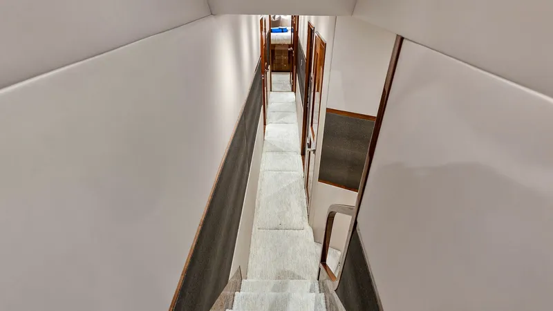 Slide: The Image of Lower Deck Stairway and Hallway This image showcases the elegant stairway leading to the lower deck of the 2017 Viking 80 Convertible. The hallway's sleek design features rich wood finishes and soft carpeting, providing a warm and inviting transition to the vessel's sleeping quarters. T - 7932660