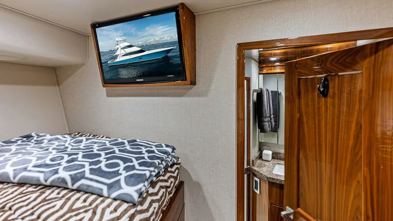 Slide: The Image of Guest Stateroom with Ensuite The guest stateroom on the Viking 80 Convertible 'Aussie Rules' features a cozy sleeping area with plush bedding and a mounted flat-screen TV for entertainment. The rich wood finishes add elegance, while the ensuite bathroom offers convenience with a mode - 7932672