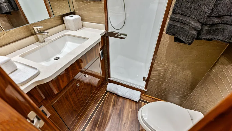 Slide: The Image of Luxurious Yacht Bathroom with Shower This elegant bathroom on the 2017 Viking 80 Convertible, 'Aussie Rules,' features exquisite wood finishes and modern fixtures. A spacious countertop with a sleek sink is paired with a glass-enclosed shower, providing both style and functionality. The warm - 7932670