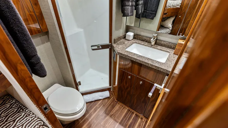 Slide: The Image of Elegant Guest Bathroom with Shower This well-appointed guest bathroom features a sleek glass-enclosed shower and a stylish vanity with a granite countertop. The warm wood cabinetry provides ample storage, while the modern fixtures enhance the space's luxurious feel. Rich wood flooring adds - 7932673