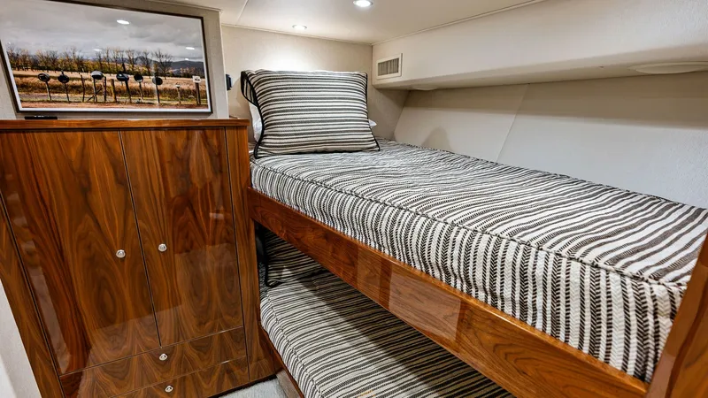 Slide: The Image of Guest Stateroom with Bunk Beds This inviting guest stateroom on the 2017 Viking 80 Convertible features stylish bunk beds with striped bedding, ideal for comfortable accommodations at sea. The space is enhanced by rich wood cabinetry offering ample storage and a modern, elegant touch. - 7932674