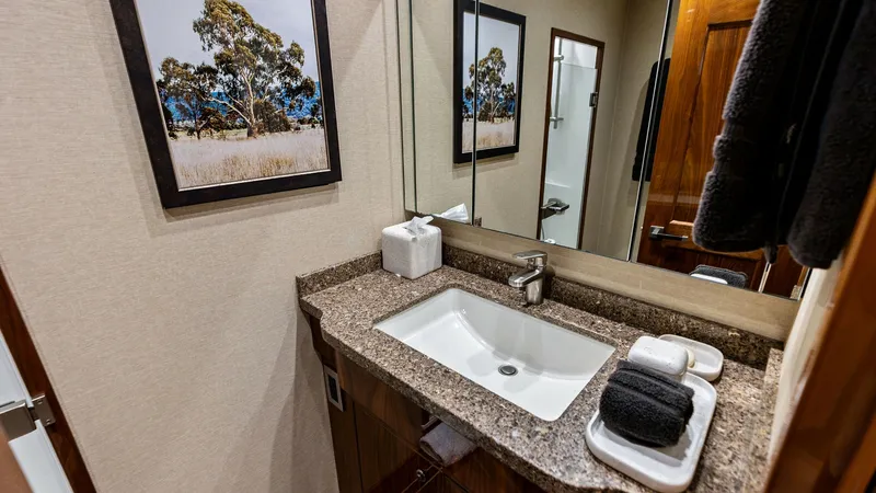 Slide: The Image of Elegant Vanity and Sink Area This sophisticated vanity area features a sleek undermount sink set within a polished granite countertop, offering both style and functionality. The rich wood cabinetry provides ample storage, complemented by a large mirrored wall that enhances the sense - 7932679