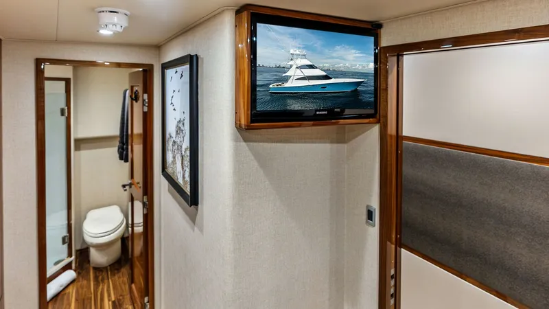 Slide: The Image of Hallway with En-Suite Bathroom Access This image showcases the well-appointed hallway of the 2017 Viking 80 Convertible, featuring sleek wood paneling and soft ambient lighting. A mounted flat-screen TV provides entertainment options, while the hallway leads to an en-suite bathroom with elega - 7932675
