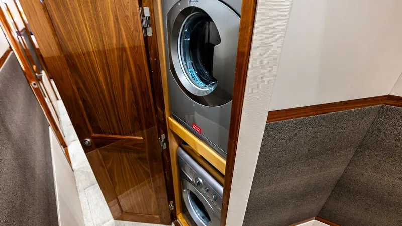 Slide: The Image of Compact Laundry Area with Appliances This image showcases the efficient laundry area on the Viking 80 Convertible, featuring a stacked washer and dryer concealed behind elegant wooden cabinetry. The high-quality wood finish adds a touch of luxury, seamlessly integrating the appliances into t - 7932662