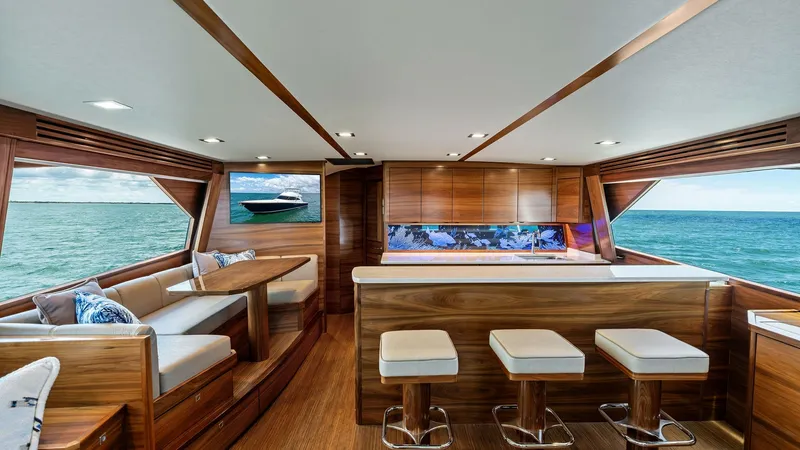 Slide: The Image of Elegant Salon with Ocean Views The salon of the 2024 Viking 68 Convertible offers a luxurious and inviting space with panoramic ocean views. Featuring rich wood finishes and plush seating, the area includes a spacious dining nook and a sleek bar with modern stools. Large windows flood - 7933119