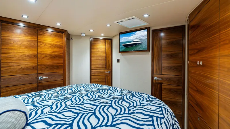 Slide: The Image of Luxurious Stateroom with Ensuite Access This elegant stateroom aboard the 2024 Viking 68 Convertible features rich wood paneling and a plush, patterned bedspread, creating a warm and inviting atmosphere. The room is equipped with a flat-screen TV for entertainment and multiple storage options, - 7933135