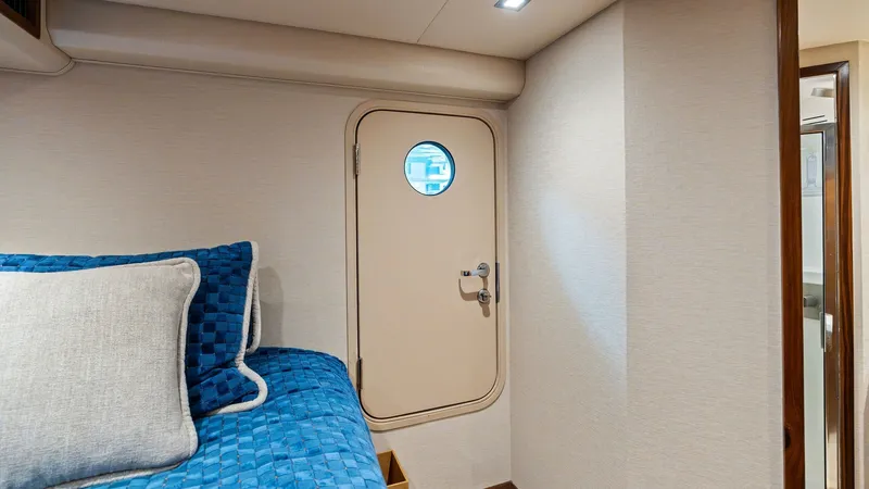 Slide: The Image of Guest Stateroom with Ensuite Access This inviting guest stateroom on the 2024 Viking 68 Convertible features a comfortable berth with plush, textured bedding in rich blue tones. The space is elegantly designed with modern lighting and seamless access to the ensuite bathroom through a stylis - 7933148