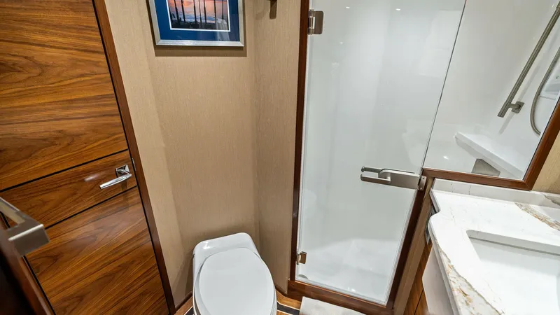 Slide: The Image of Luxurious En-Suite Bathroom This elegant en-suite bathroom on the 2024 Viking 68 Convertible features high-end finishes, including rich wood cabinetry and a sleek glass shower enclosure. The space is beautifully appointed with a modern, polished countertop and a framed artwork, addi - 7933147