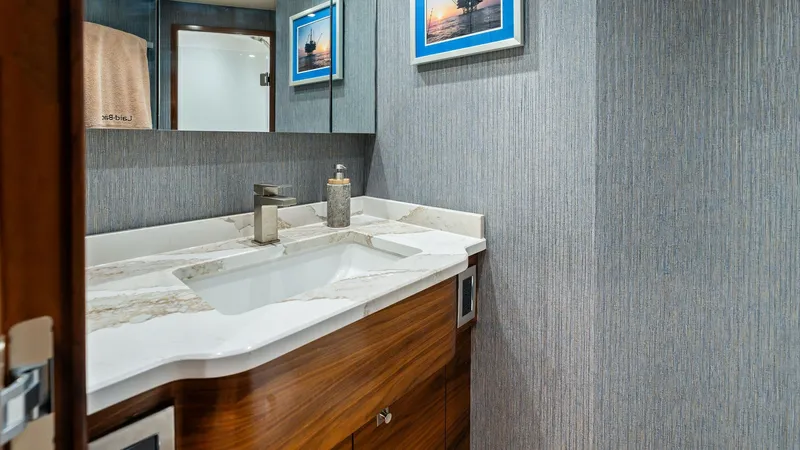 Slide: The Image of Guest Bathroom with Modern Vanity This elegant guest bathroom on the 2024 Viking 68 Convertible features a sleek, modern vanity with a polished marble countertop. Rich wood cabinetry adds warmth and sophistication, while the textured wall coverings provide a contemporary touch. The well-p - 7933139