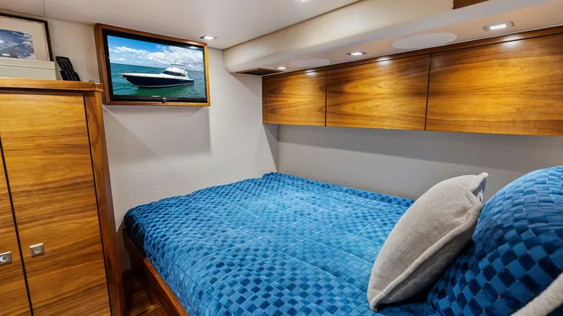 Slide: The Image of Guest Stateroom with TV This cozy guest stateroom features a plush double bed adorned with a vibrant blue quilt, providing a relaxing retreat. The space is accentuated by rich wood cabinetry offering ample storage and a mounted flat-screen TV for entertainment. Recessed lighting - 7933144