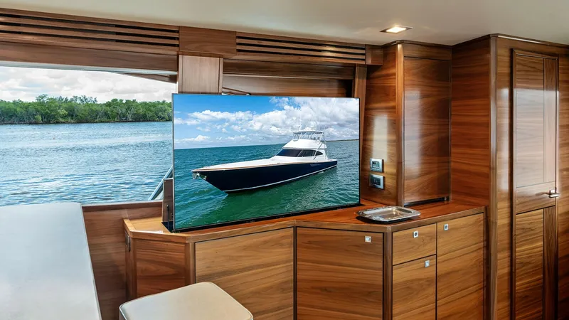 Slide: The Image of Salon with Pop-Up TV Feature The salon of the 2024 Viking 68 Convertible offers luxurious comfort with its rich wood cabinetry and sleek design. A pop-up TV enhances entertainment options, seamlessly integrated into the space without disrupting the elegant aesthetic. Large windows pr - 7933123