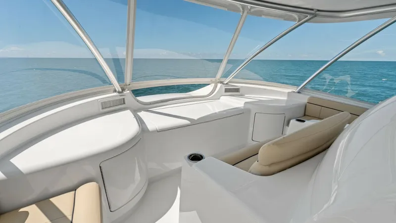 Slide: The Image of Flybridge Helm Seating Area This image showcases the flybridge helm seating area of the 2024 Viking 68 Convertible. The spacious layout offers plush, beige seating with panoramic ocean views through large, wrap-around windows. The sleek, white finishes and ergonomic design make this - 7933164