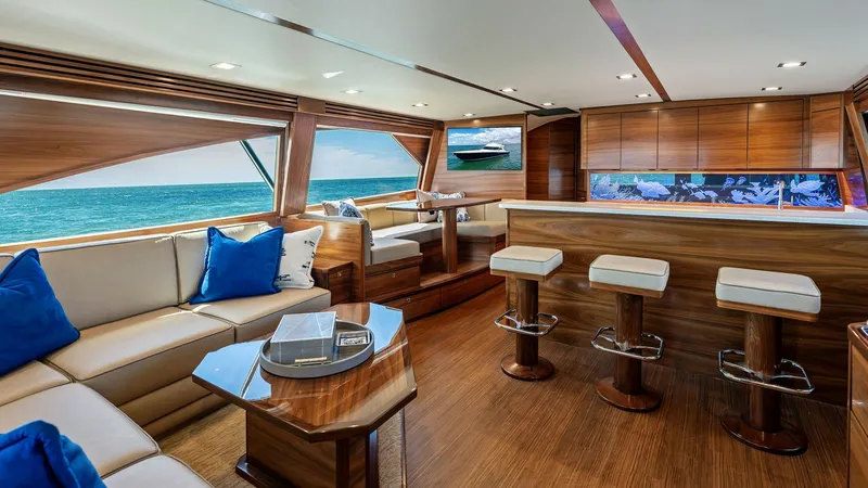 Slide: The Image of Spacious Salon with Ocean Views The salon of the 2024 Viking 68 Convertible exudes luxury with its rich wood finishes and expansive ocean views through large windows. Featuring comfortable seating, a sleek bar with modern stools, and a dining area, this space is perfect for entertaining - 7933126