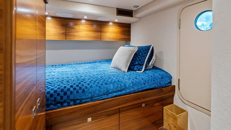 Slide: The Image of Guest Stateroom with Porthole View This cozy guest stateroom on the 2024 Viking 68 Convertible features a plush bed adorned with a vibrant blue quilt and accent pillows. The rich wood cabinetry offers ample storage and complements the elegant finishes throughout the space. A porthole provi - 7933145