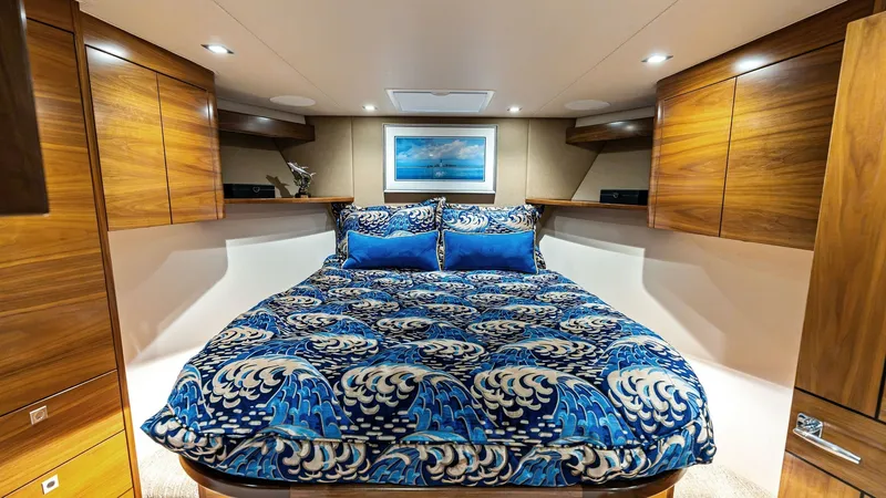 Slide: The Image of Luxurious Forward Stateroom Interior This forward stateroom on the 2024 Viking 68 Convertible offers a blend of comfort and style, featuring a plush double berth adorned with an elegant wave-patterned bedspread. The warm wood cabinetry provides ample storage, complemented by soft, recessed l - 7933137