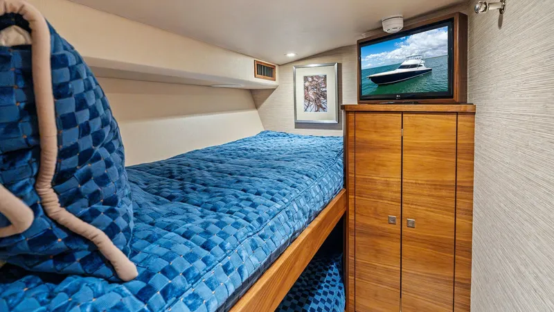 Slide: The Image of Guest Stateroom with Bunk Beds This cozy guest stateroom on the 2024 Viking 68 Convertible features stylish bunk beds adorned with plush blue bedding, providing comfort and elegance. The room is equipped with a sleek wooden cabinet for ample storage, and a mounted TV for entertainment. - 7933141